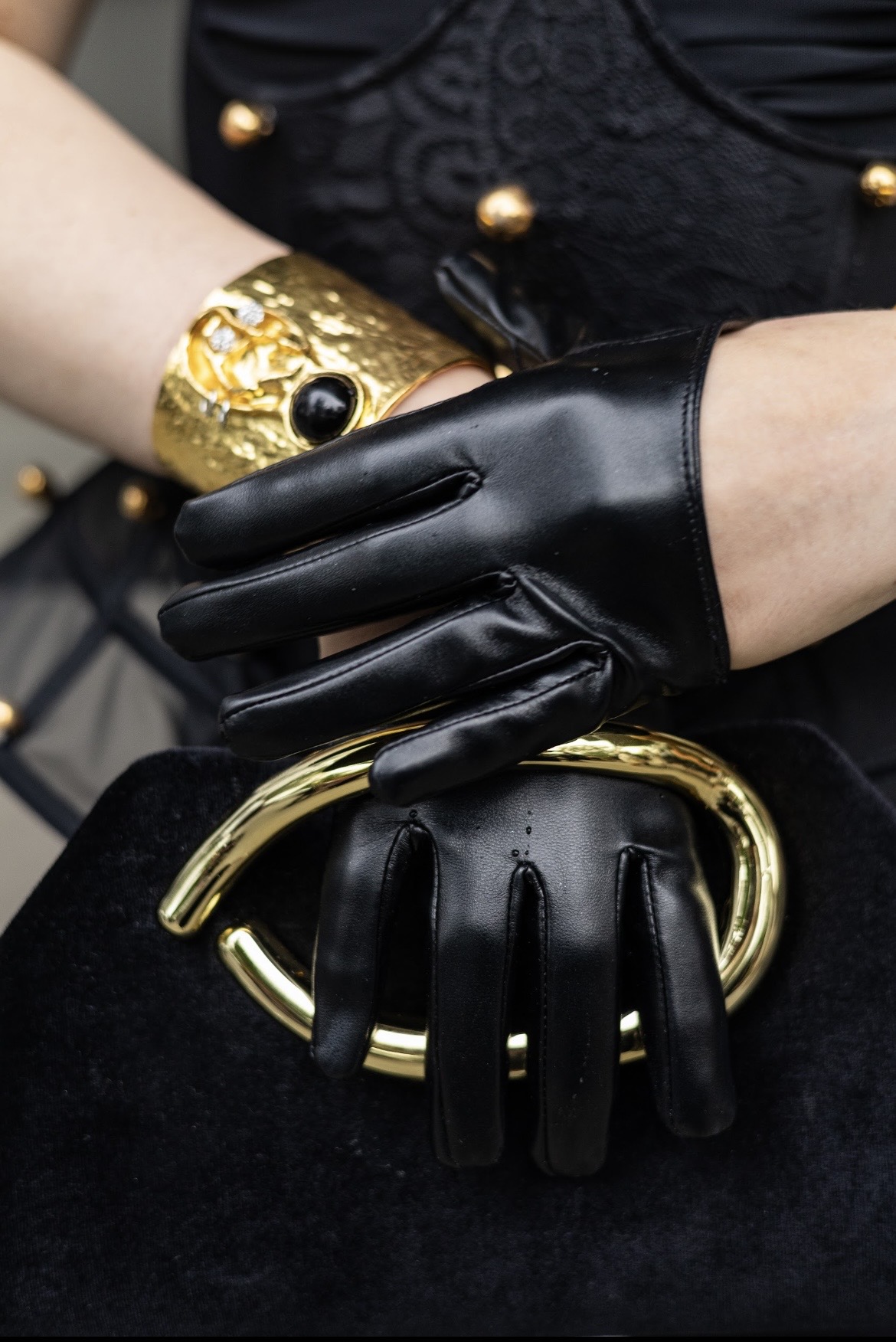 Detail of black leather gloves and gold cuff jewellery