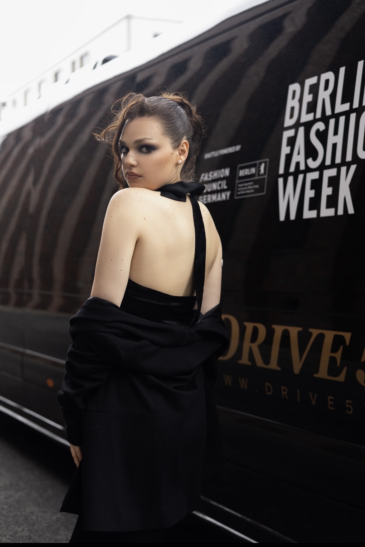 Adeline Frickel in a black backless gown beside a Berlin Fashion Week shuttle