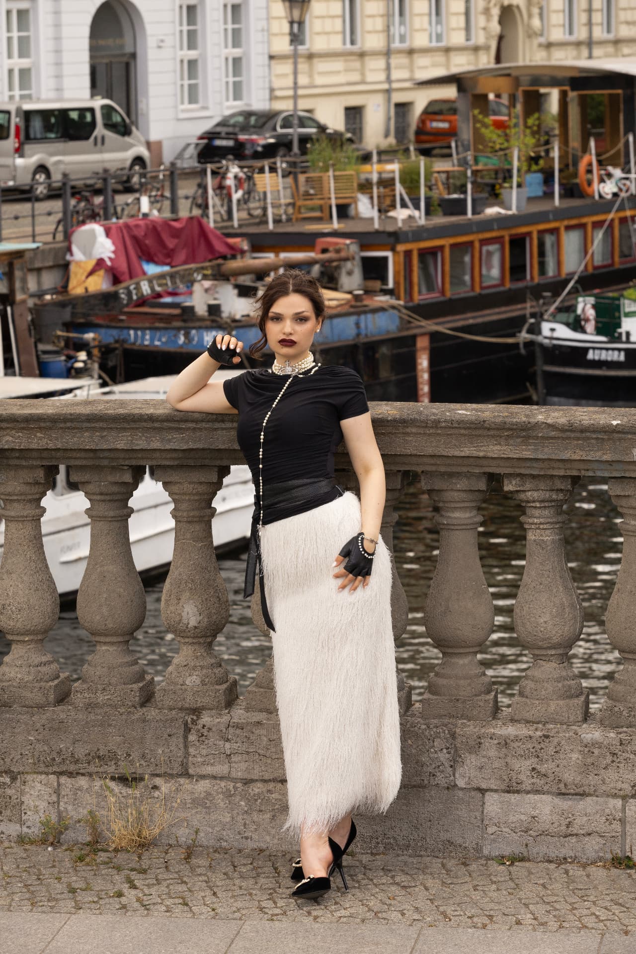 Adeline Frickel in a black top and white fringed skirt beside a Berlin canal